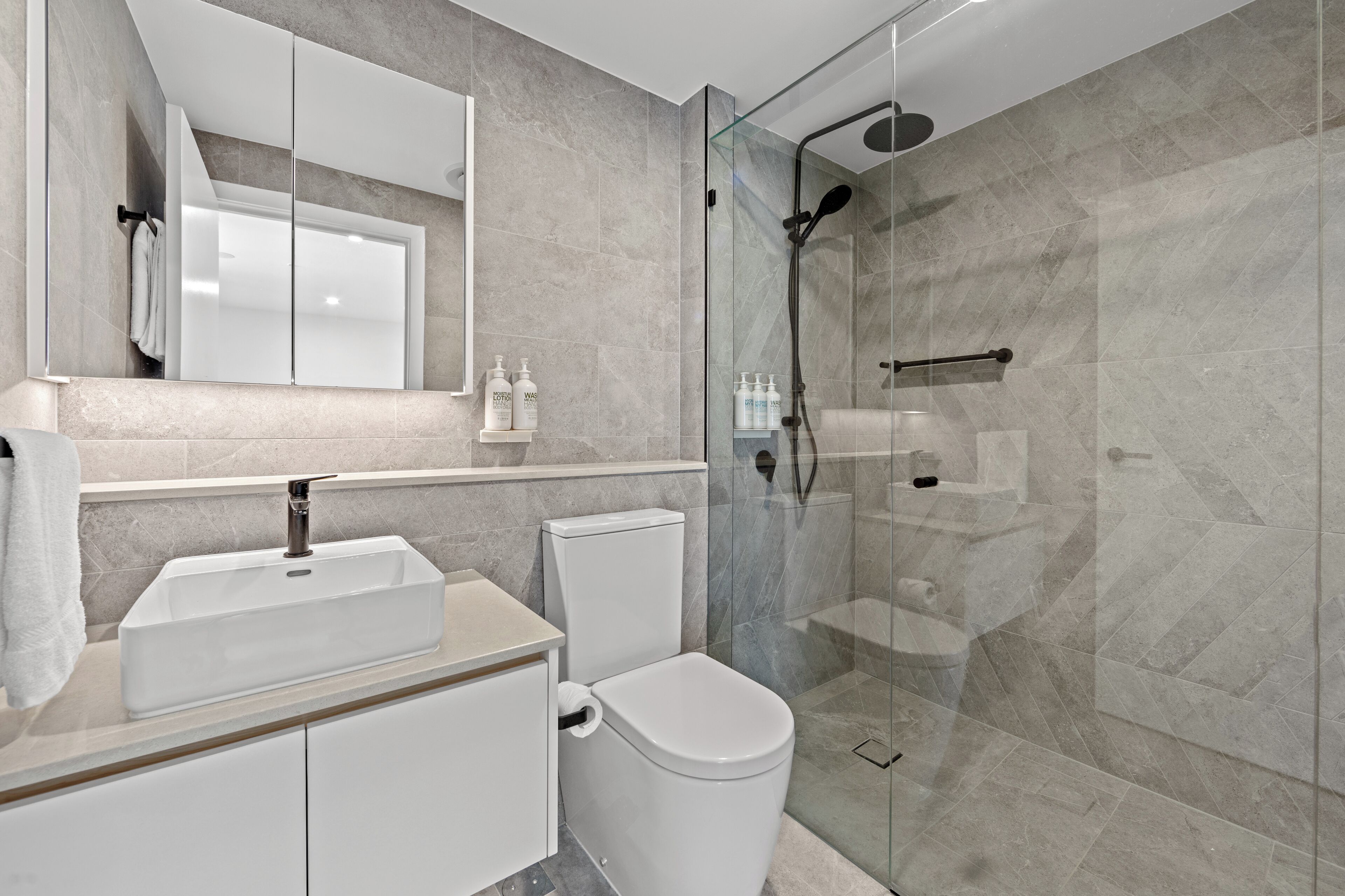 A modern bathroom with a glass-enclosed shower, a white sink, and a toilet.