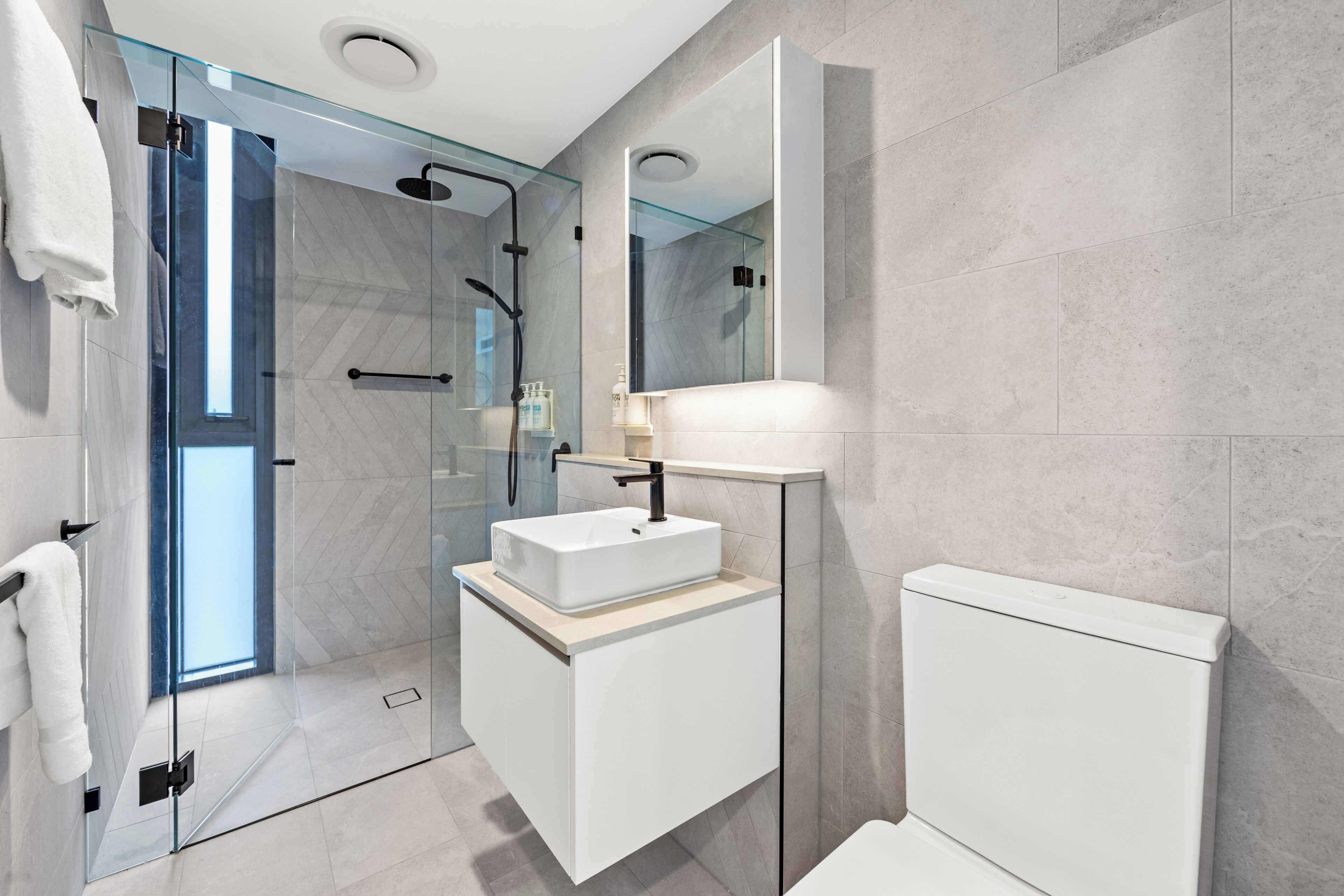Een moderne badkamer met een douchecabine van glas, een wit wastafelmeubel en een toilet.