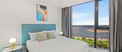A modern bedroom with a large bed, a ceiling fan, and a view of a body of water through large windows.