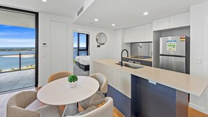 A modern kitchen with a built-in island, a large window with a view of the sea, and a dining area with a round table and chairs. - Marine Quarter Apartments by CLLIX (Southport)