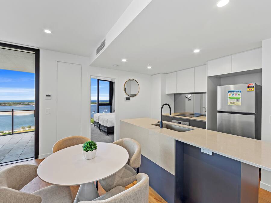 Een moderne keuken met een inbouw kookeiland, een groot raam met uitzicht op zee, en een eethoek met een ronde tafel en stoelen.