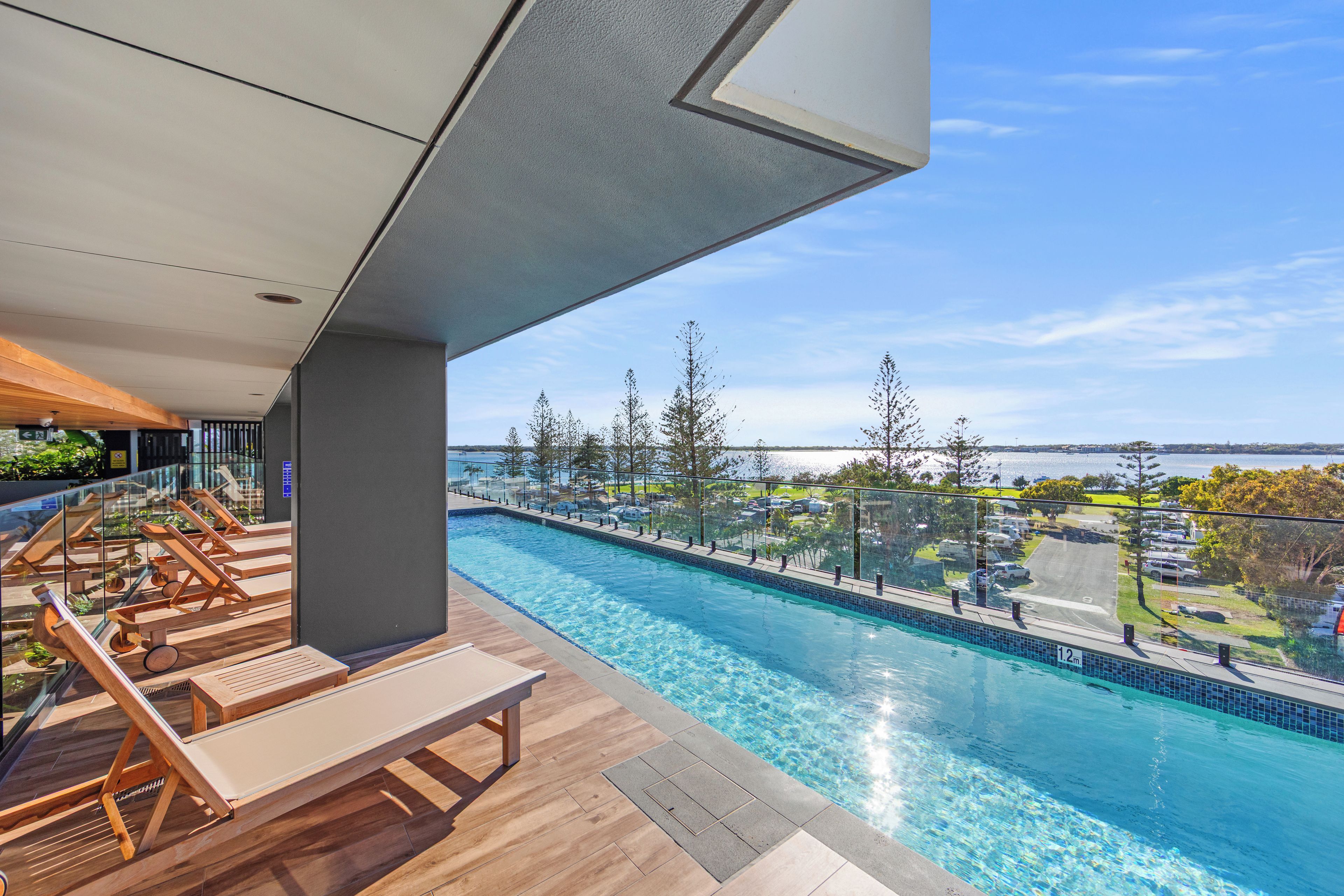 A modern outdoor pool area with lounge chairs and a view of a body of water.