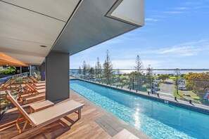 A modern outdoor pool area with lounge chairs and a view of a body of water. - Marine Quarter Apartments by CLLIX (Southport)