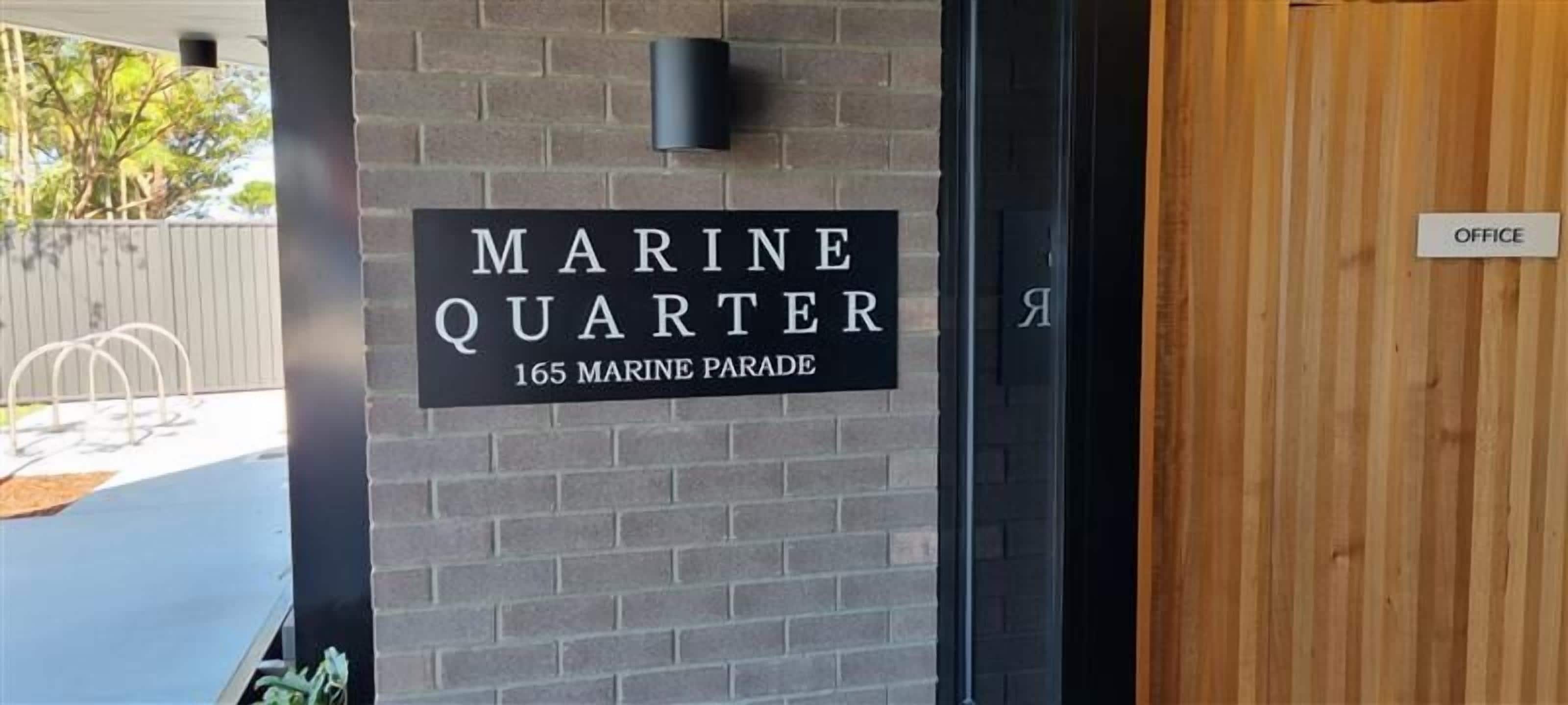Een bord met de tekst 'MARINE QUARTER 165 MARINE PARADE', rechts ervan een houten deur met daarop 'KANTOR'.