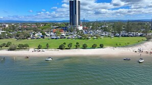 A coastal area with a large building, a grassy field, and a beach. - Marine Quarter Apartments by CLLIX (Southport)