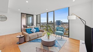 A modern living room with a sofa, armchairs, a coffee table, and a large window offering a city view. - Marine Quarter Apartments by CLLIX (Southport)