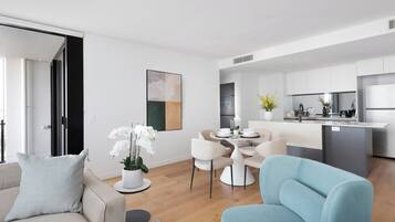 A modern living room with a sofa, a dining table with chairs, and a kitchen area with a refrigerator and cabinets.