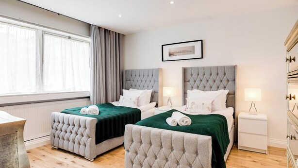 A hotel room with two beds, a bedside table, a lamp, and a framed picture on the wall. - 4 Bedroom Villa on Marble Arch (London)