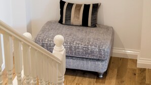 A staircase with a white railing leading to a landing. Below, a gray bench with a striped cushion is placed against a white wall. A framed artwork of a red flower is hung above the bench. - 4 Bedroom Villa on Marble Arch (London)