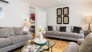 A modern living room with two grey sofas, a glass coffee table, and a vase with white flowers. - 4 Bedroom Villa on Marble Arch (London)