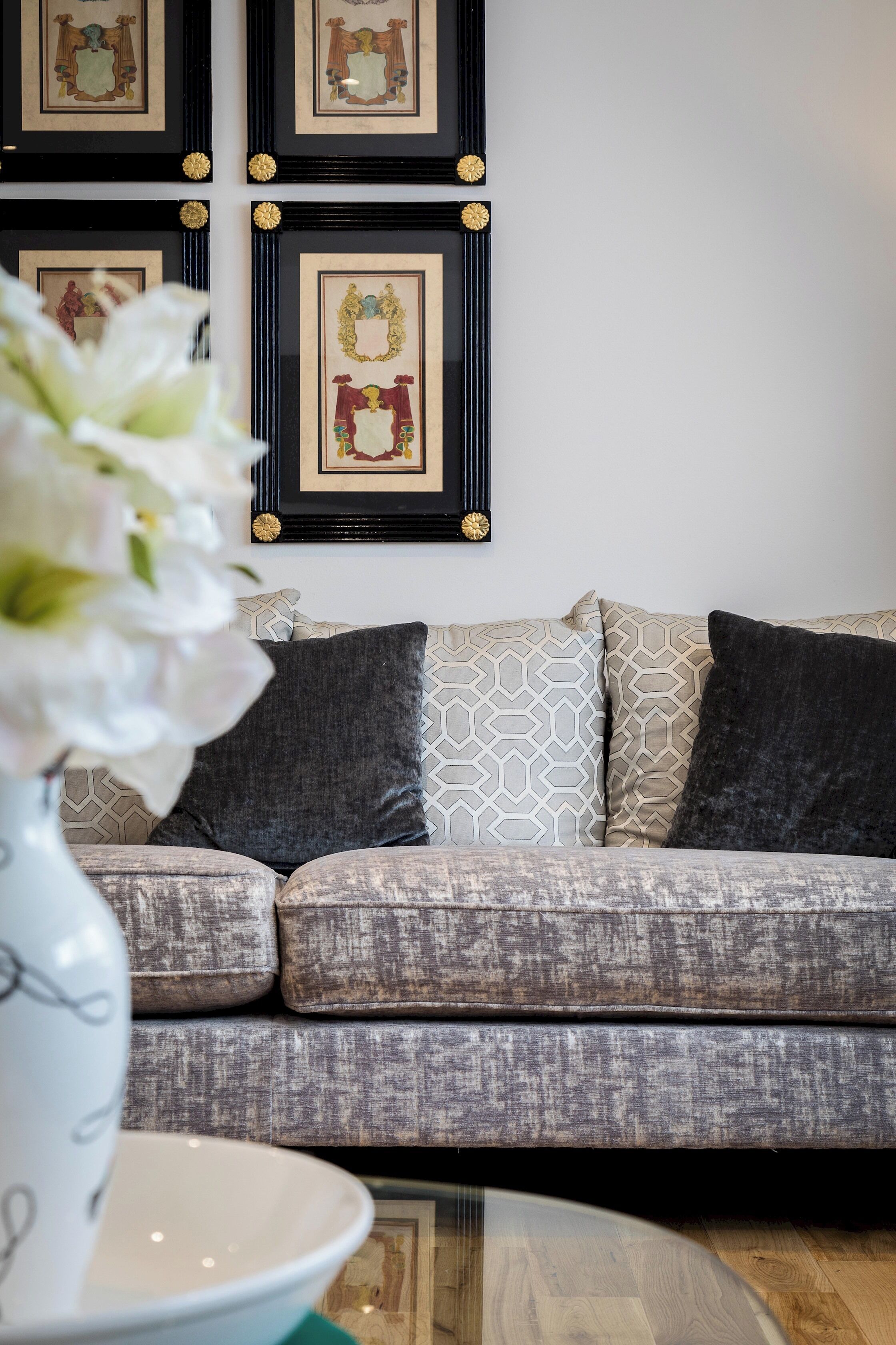 Een woonkamer met een grijze gestreepte bank, een witte vaas met bloemen en lijstwerken aan de muur.