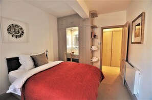 A bedroom with a bed, a wardrobe, a mirror, and a door leading to another room.