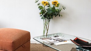 A room with a painting of a beach scene, a glass table with a vase of sunflowers, and a brown armchair. - Penthouse With Views Across London (London)