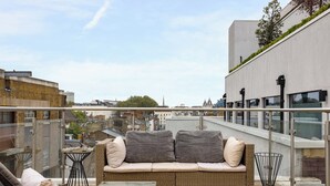 A balcony with wicker furniture, a glass railing, and a city view. - Penthouse With Views Across London (London)