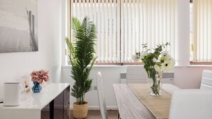 A modern living room with a white sofa, a wooden dining table, a white coffee table, a large potted plant, and a vase with flowers. - Penthouse With Views Across London (London)