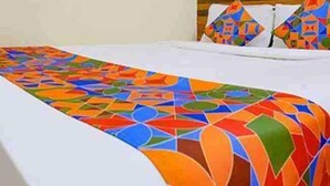 A bed with a colorful geometric-patterned bedspread, a wooden headboard, and a wall with a wooden wall art piece. - Diamond By Glitz Hotels (Mumbai)