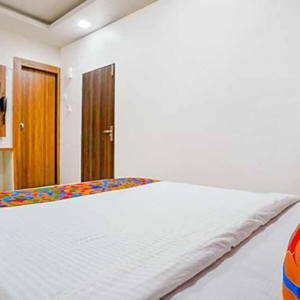 A hotel room with a bed, a wooden door, and a white wall.