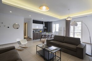 Uma sala de estar moderna com um sofá, uma mesa de centro de vidro e uma área de jantar com mesa e cadeiras.