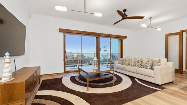 Ein modernes Wohnzimmer mit großem Fenster, Deckenventilator und weißem Sofa mit gemusterten Kissen.