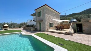 En villa i sten med en swimmingpool, utomhusmöbler och utsikt över det omgivande landskapet.