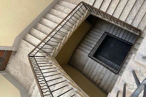 A spiral staircase with a metal railing, a small window at the top, and a beige wall.