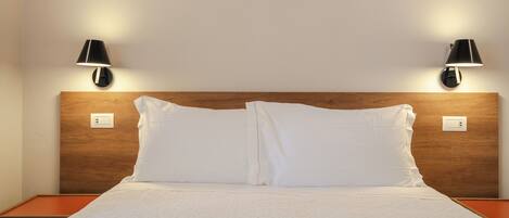 A neatly made bed with white linens, two bedside lamps, and a wooden headboard.