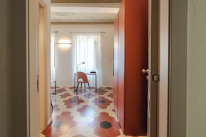 A hallway with a patterned floor, a desk with a chair, and a door. - AmiRooms Affittacamere (Siena)