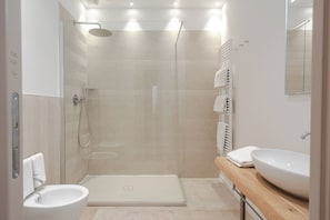 A modern bathroom with a glass-enclosed shower, a white sink, and a wooden vanity. - AmiRooms Affittacamere (Siena)