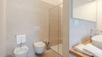 A modern bathroom with a bidet, toilet, glass shower enclosure, and a sink with a mirror.