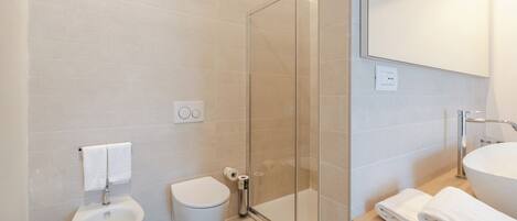 A modern bathroom with a bidet, toilet, glass shower enclosure, and a sink with a mirror.