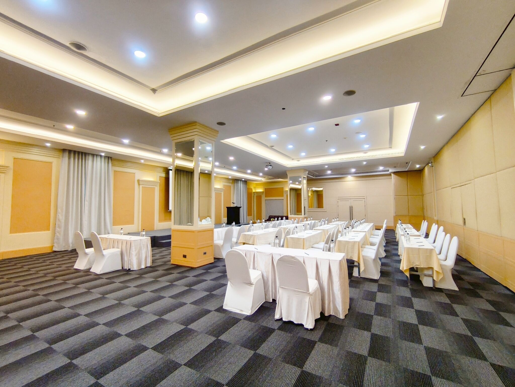 A conference room with multiple tables and chairs, a podium, and a large mirror.