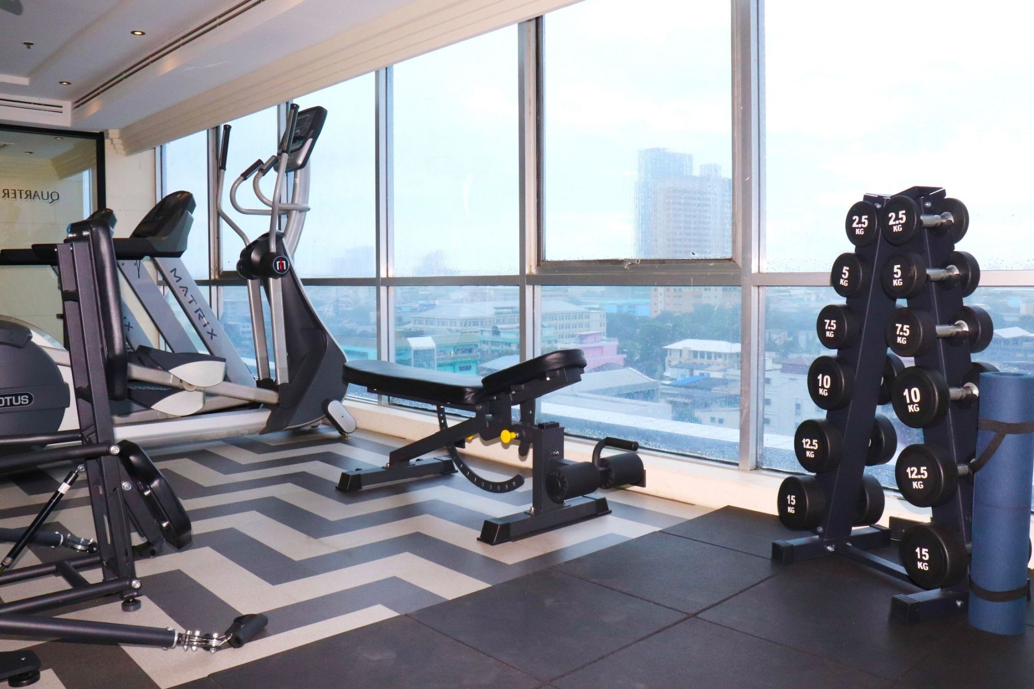 Een fitnessruimte met cardioapparatuur, gewichthefmaterialen en een uitzicht op de stad door grote ramen.
