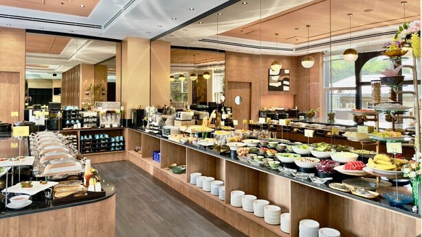 Un buffet de petit-déjeuner moderne proposant une grande variété de plats, un espace pour s’asseoir et une cuisine en arrière-plan.