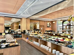 Ein modernes Frühstücksbuffet mit vielfältigen Speisen, einer Sitzgelegenheit und einer Küche im Hintergrund.