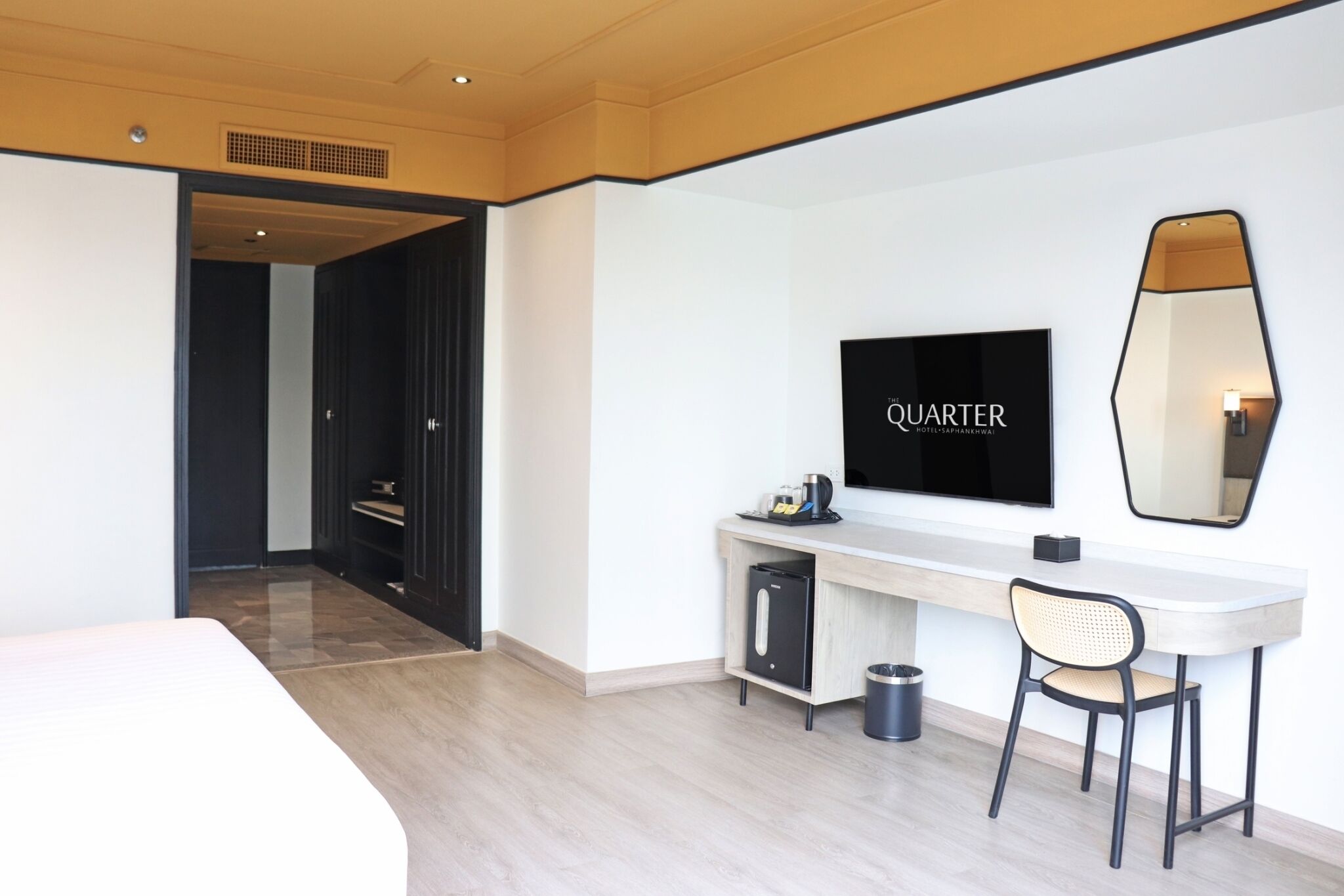 A modern hotel room with a large bed, a desk with a chair, a TV mounted on the wall, and a mirror.
