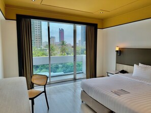 Une chambre d’hôtel avec un grand lit, une chaise, une table de chevet et une vue sur le paysage urbain, visible à travers une grande fenêtre.
