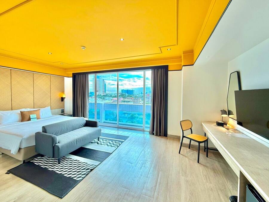 A hotel room with a bed, a sofa, a desk, a chair, and a large window offering a city view.
