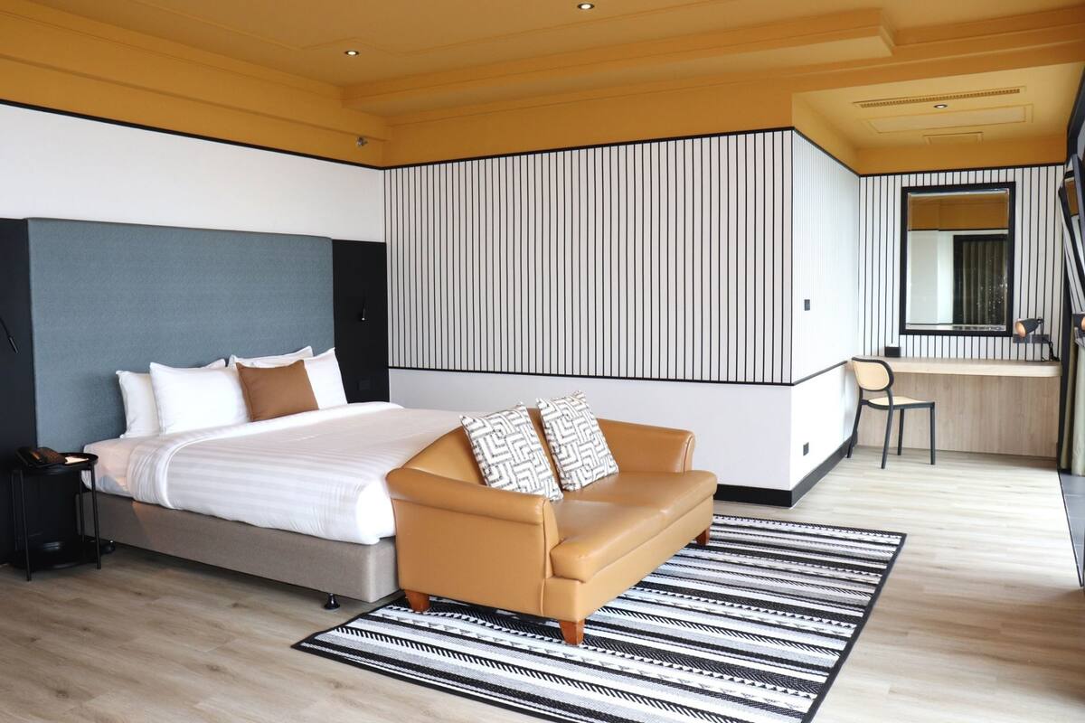 Una habitación de hotel moderna con una cama grande, un sofá, un escritorio y un espejo.
