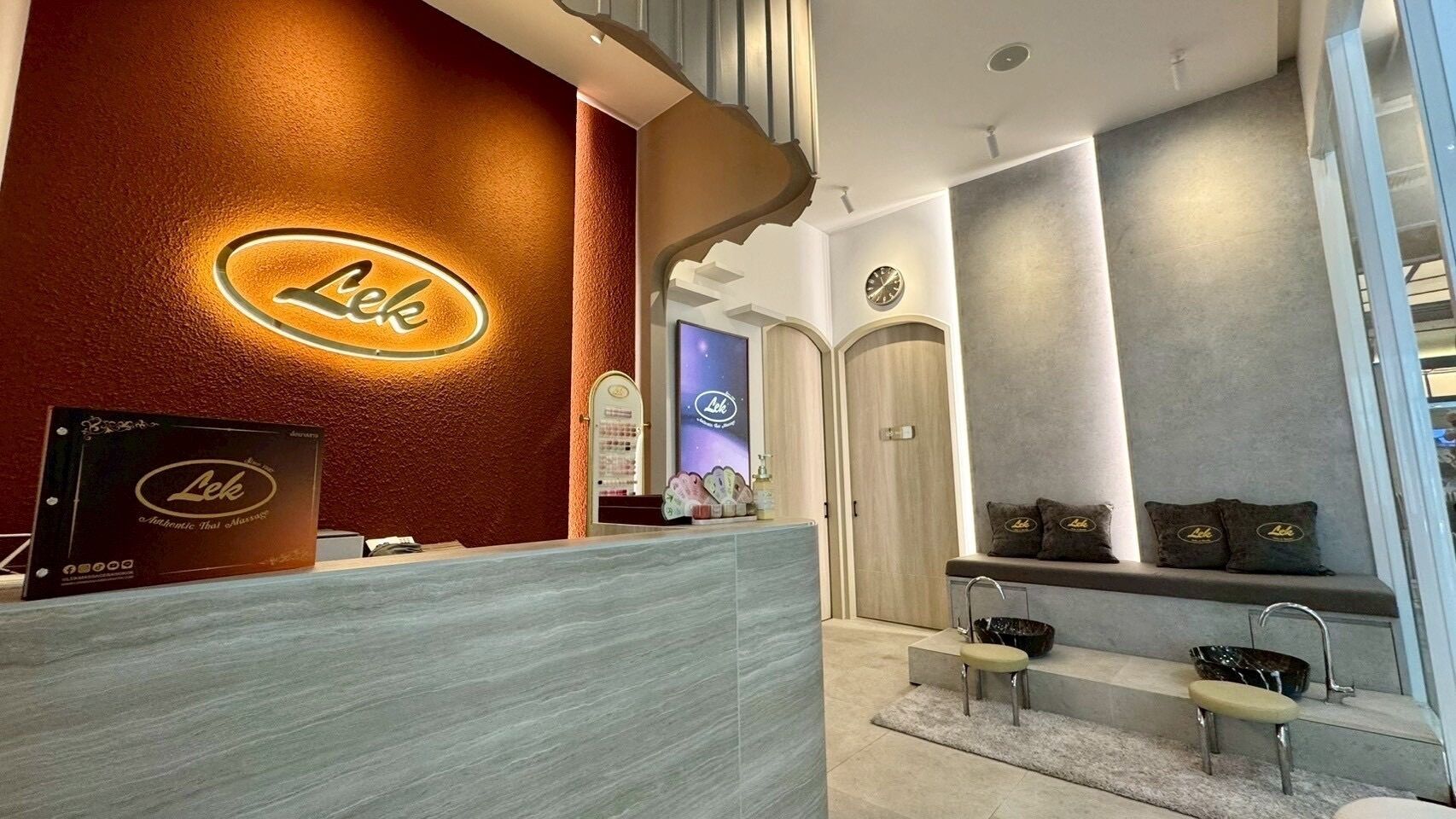 Zona de recepción con pared de madera y un letrero que dice "Lek". Hay un mostrador de recepción, un banco y un rincón con cojines.