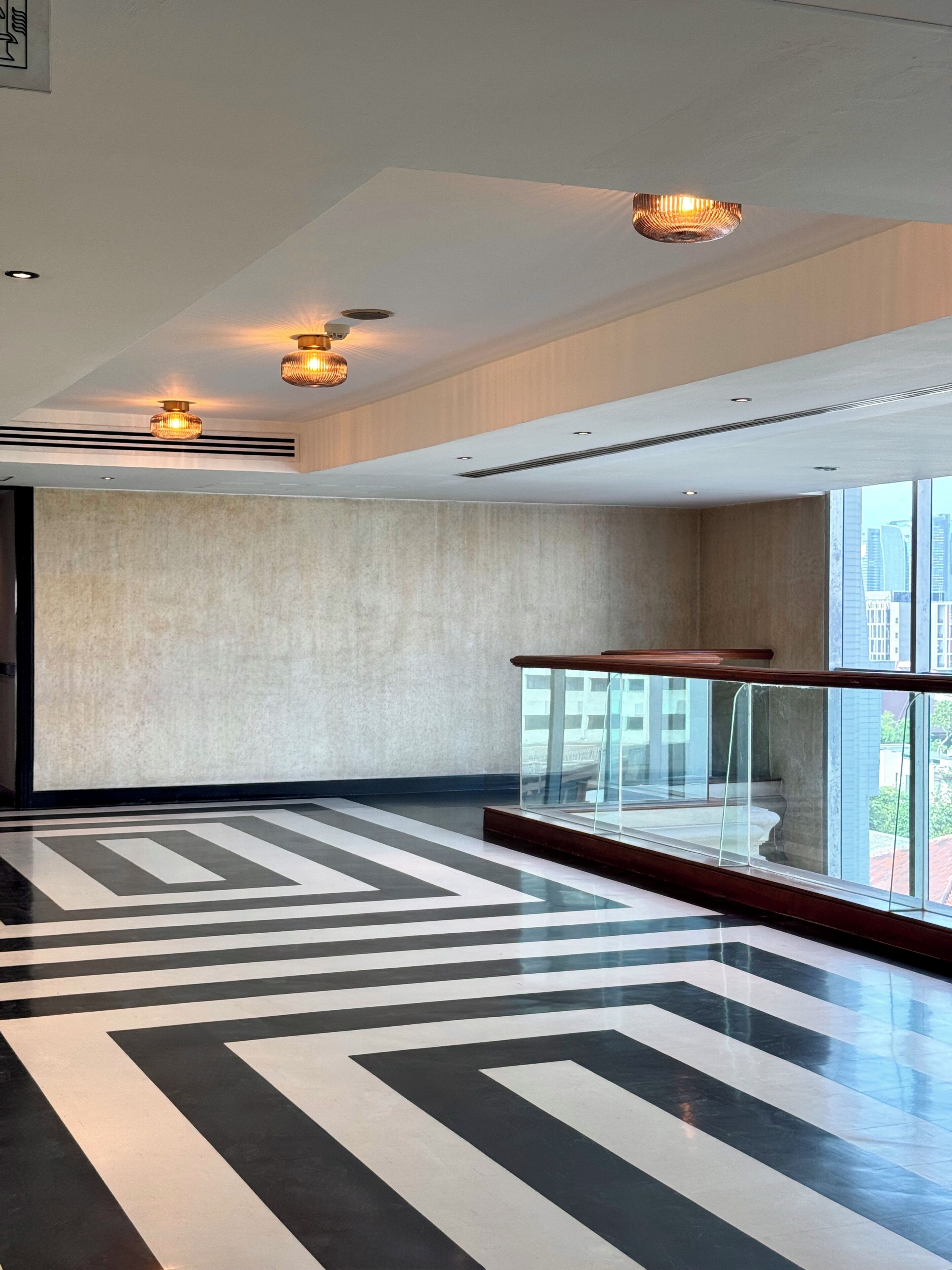 A spacious lobby with a geometric patterned floor, a glass railing, and recessed lighting.