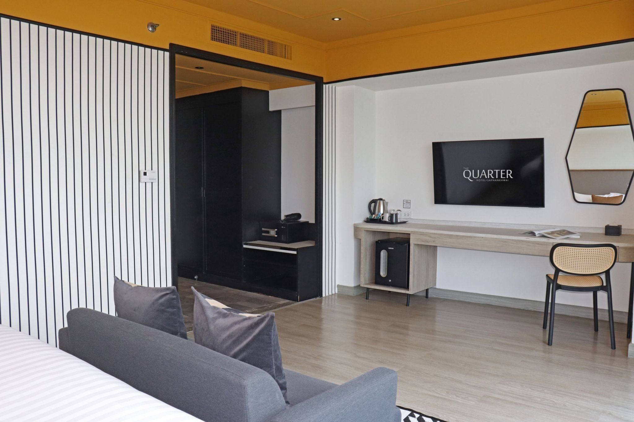 A modern hotel room with a bed, a desk, a chair, a TV, and a minibar.