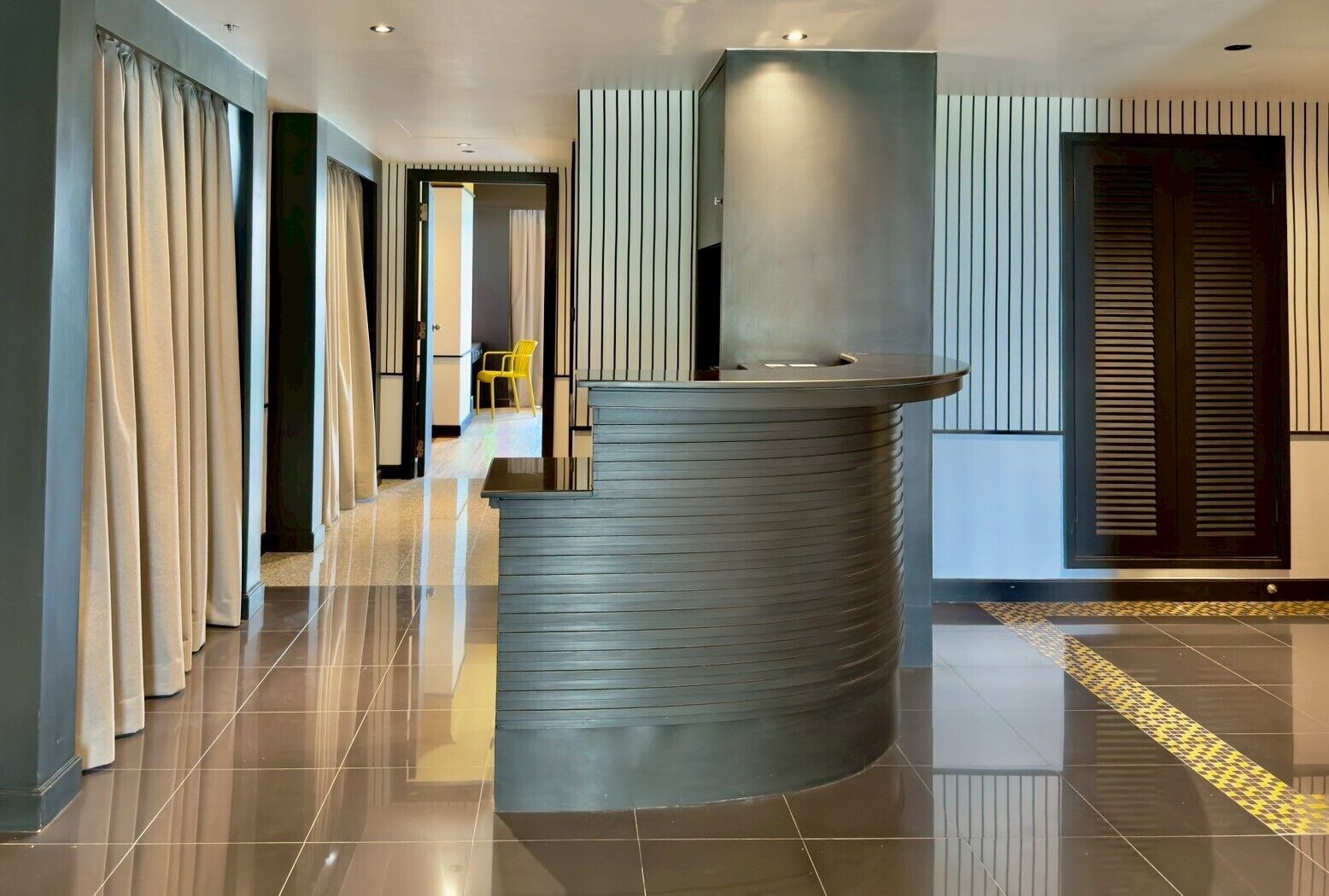 A modern reception area with a curved counter, a chair, and a door with vertical blinds.