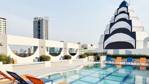 Un espace piscine sur le toit, doté d’une piscine au design moderne, de chaises longues et d’un bâtiment remarquable en arrière-plan.