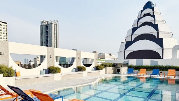 Un área de piscina en la azotea con un diseño moderno, sillas de descanso y un edificio distintivo al fondo.