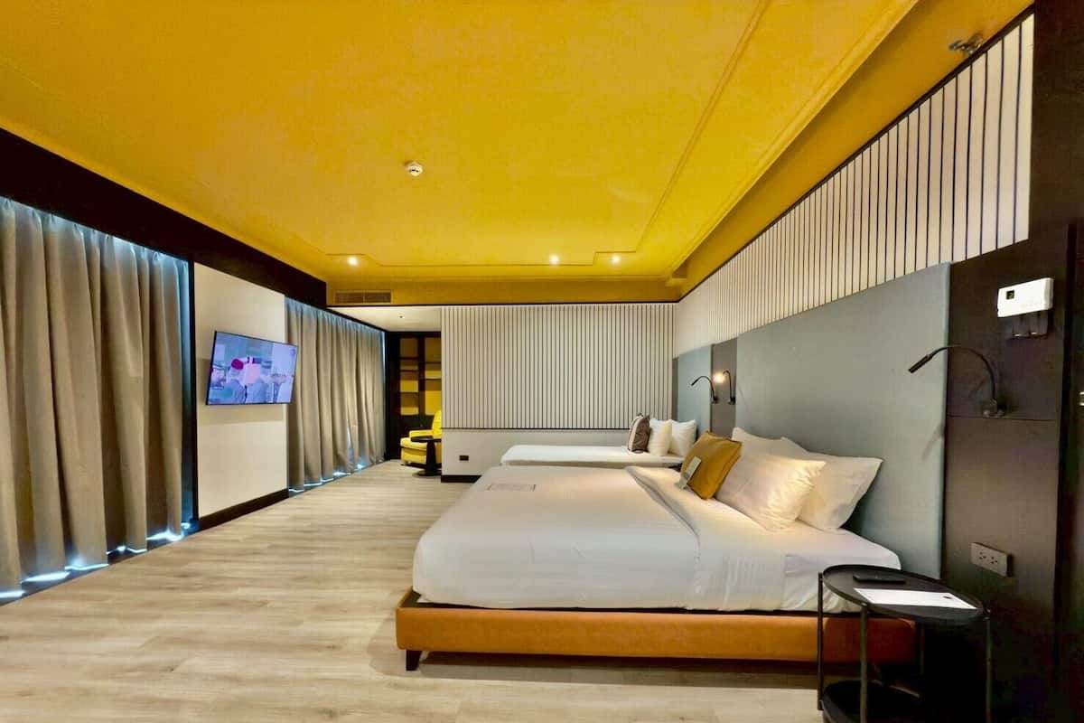 Una habitación de hotel moderna con una cama grande, un televisor en la pared y un pequeño rincón de estar con una silla amarilla.