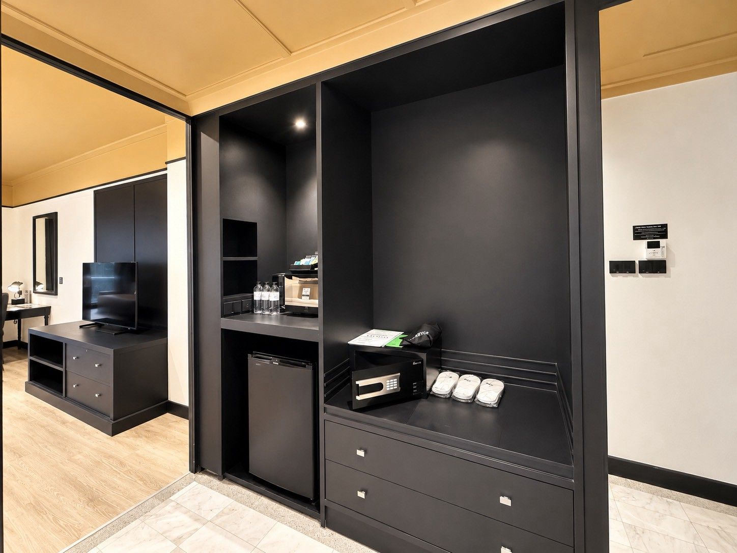 A modern hotel room with a large black entertainment unit, a flat-screen TV, and a minibar.