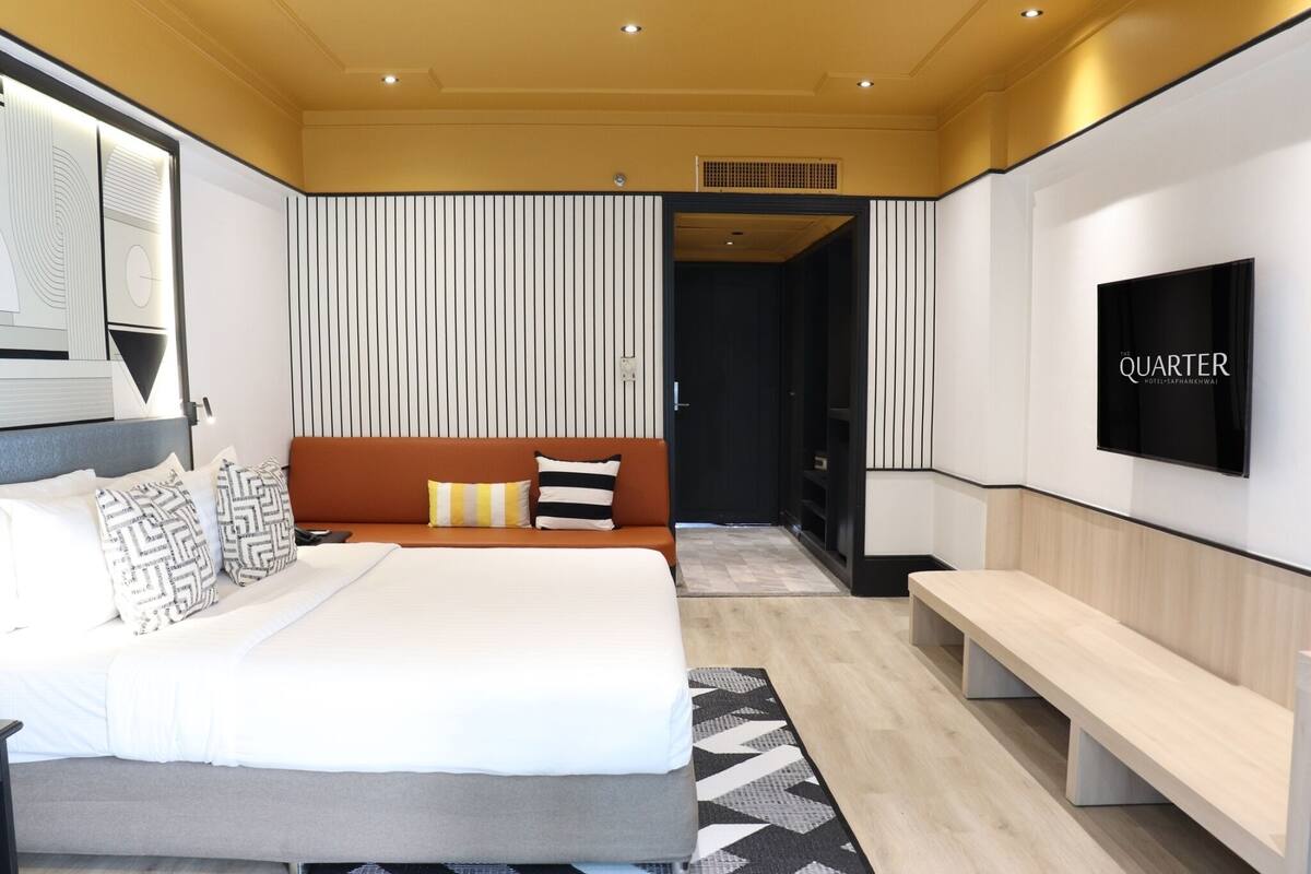 Una habitación de hotel moderna con una cama grande, un sofá, un banco y un televisor en la pared.