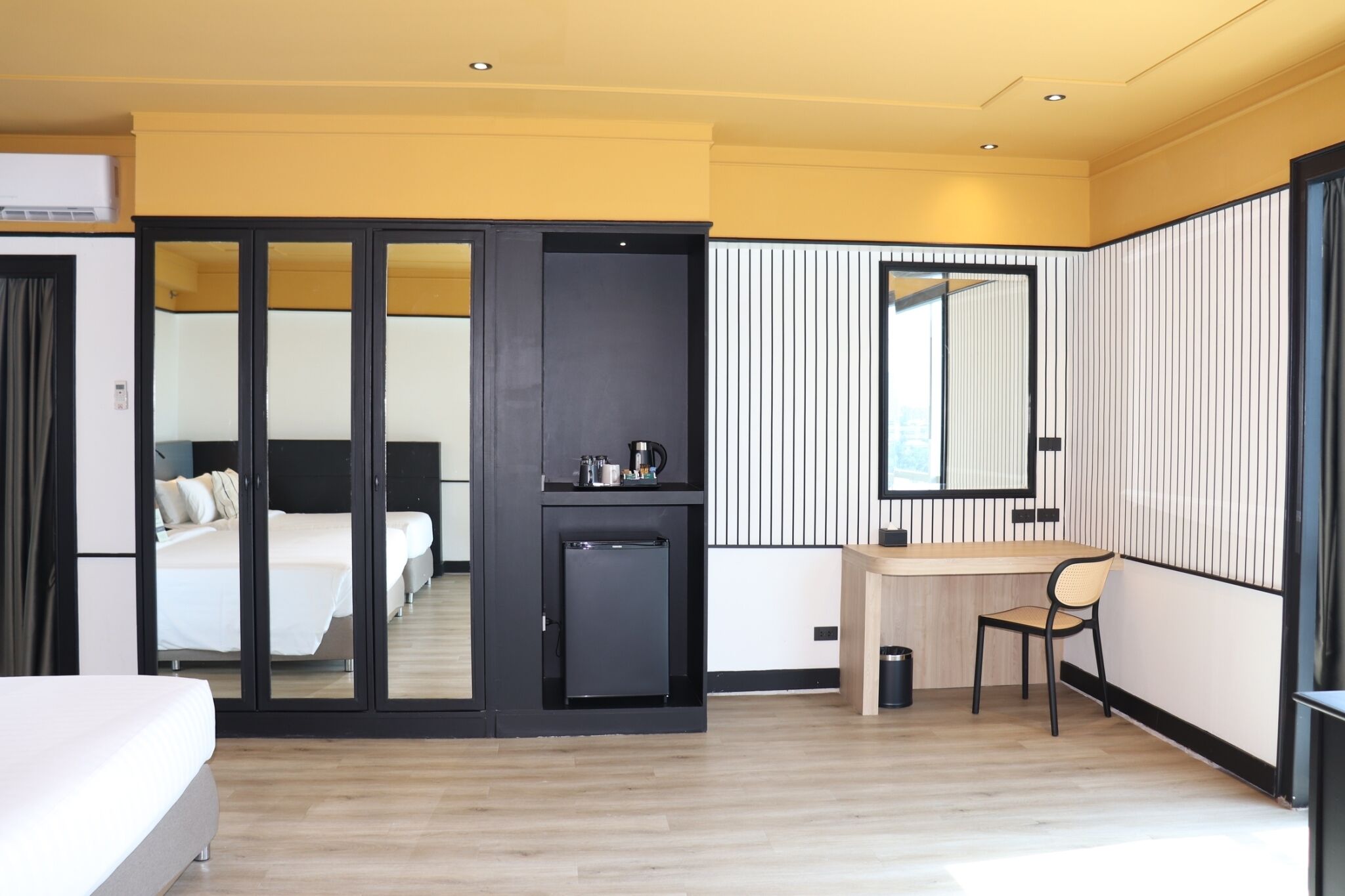 Ein modernes Hotelzimmer mit einem Bett, einem Schreibtisch, einem Stuhl, einem kleinen Kühlschrank und einem Spiegel.