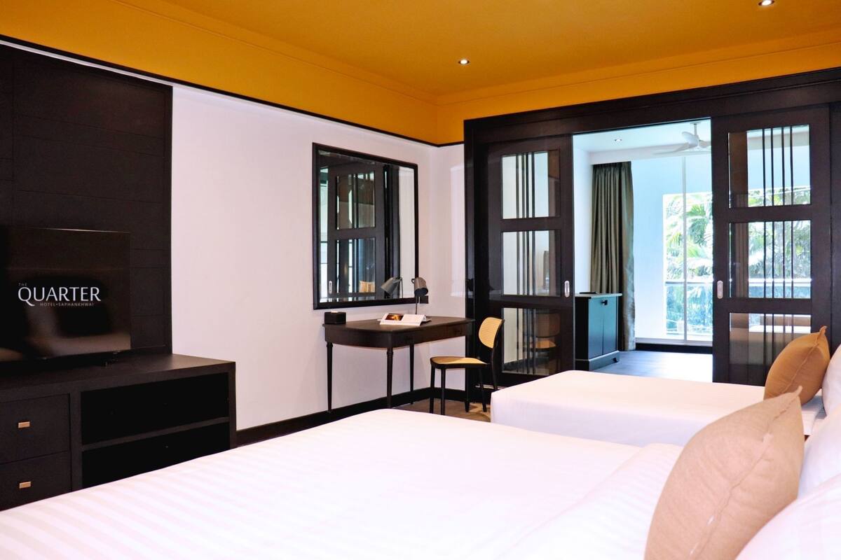 Habitación de hotel con dos camas, un escritorio, una silla, un televisor y ventanas amplias.