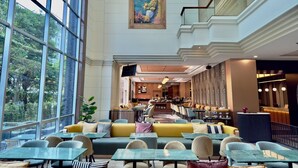 Un espacio interior amplio con ventanas grandes, una zona de comedor con mesas y sillas, y una zona de bar o sala de estar.